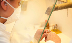 Zahntechnikerin arbeitet mit Mundschutz an Zahnprothese im zahntechnischen Labor.